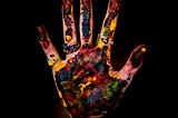 A hand, held up, palm facing, covered in paint, on a black background.