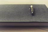 Black pen laying flat on top of Black hardback book