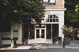 A storefront on a street corner, with a tree partially obscuring a window