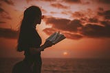 a woman reading against a red sunset