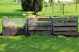 three wooden compost bins in a grassy yard