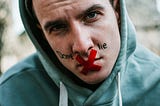 Coloured image showing a young man wearing a light green hoody. His lips are taped with a red X and the words don’t lie are written on his face, one word on each side of his nose.