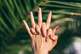 One hand holding the other in front of a palm tree leaf.