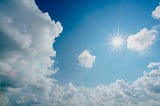 Blue sky with puffy clouds with dazzling sun image