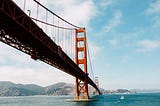 Golden Gate bridge over blue water of San Francisco Bay, with Marin headlands in the distance.