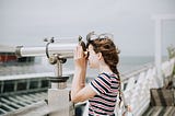 Young girl looks out to sea through binoculars on a pier