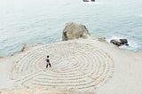 A person find a path through a maze created with stones on a beach