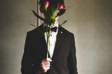 A man in a suit stands holding flowers up to his face.