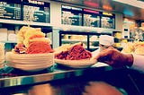 Two pastrami sandwiches stacked high on a deli counter.