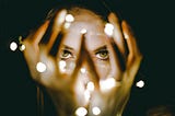 woman looking through her hands. with lights in them.