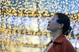 A woman wearing futuristic glasses staring upwards, while behind her there is a wall of lifts