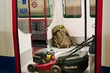 A lawnmower on a train that Rabbit Man took along with his backpack full of his stuff.