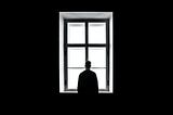 A man in a dark room stands in silhouette at a window