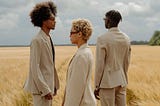 Three people standing on a rye field, all looking in different directions.