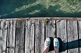sneakered feet on a faded dock above water
