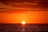 Hopeful sunrise over the ocean with a sailboat on the horizon
