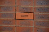 The word courage written on a brick wall.
