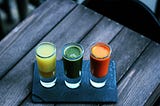 three glasses with healthy protein drinks, one yellow, one green and one orange