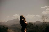 woman standing outside, facing the sky and mountains