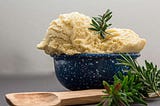 a bowl of vanilla ice cream with a sprig of rosemary and a wooden spoon nearby.