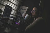 A person sitting at a laptop in a dark room. They look sad.