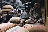 A man sitting on the gunny bags in a busy indian market street.