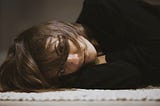 A woman with dark hair and wearing a black jumper lying on the floor, her hair across her face.