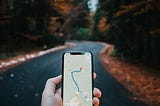 Phone screen showing a highlighted path on a navigation app. Tree-lined street in the background