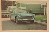 Old green Austin Healey convertible parked in front of a mobile home