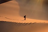 a solitary person walking in the desert sand dnes