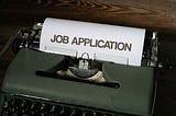 Typewriter with a paper in it, showing the words “Job Application”