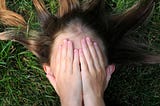 girl lying on grass with hands covering her eyes