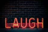 an illuminated red and yellow neon sign of the word LAUGH against a brick wall background