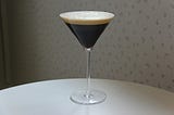 A dark brown, almost black liquid in a martini glass