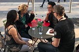 4 people engaged in conversation around a very tiny table.