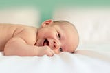 A photo of a smiling baby lying on a white blanket