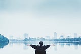 Woman looking across a lake at a skyline.