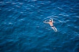 Aerial view of a older man swimming alone in a deep blue sea