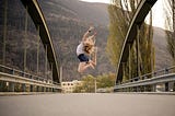 woman jumping up in the air on a bridge