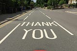 A road marked with the words in caps: “Thank You”, with a seven-coloured rainbow under them