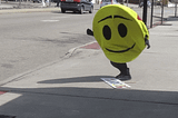 GIF of a person wearing a smiley face costume and falling on the ground