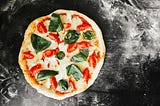 A pizza with sliced tomatoes and basil on a dusted black countertop