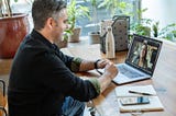 Man on a video chat sat at a desk with his laptop