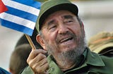 Fidel Castro in close-up, in military fatigues, laughing, and waving a small Cuban flag