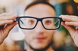 A man holding his eye glasses in front of his face, which is blurred
