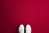 A pair of visible white trainers on a red carpeted background