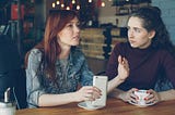 Two women sitting in a coffee shop chatting.
