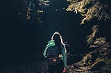 Photo of a loan woman wearing a backpack hiking uphill in a forrest.