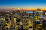 A sunset sky behind the New York City skyline lit up for the night