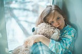 Sick little girl stuck at home hugging a teddy bear.